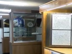 Cabinets in a school Legacy Center, displaying memorabilia from the school's history. In the back are two cabinets with mascot heads, dishes, and other items. In the foreground and to the right is a display of past yearbooks, illuminated by LED lighting.